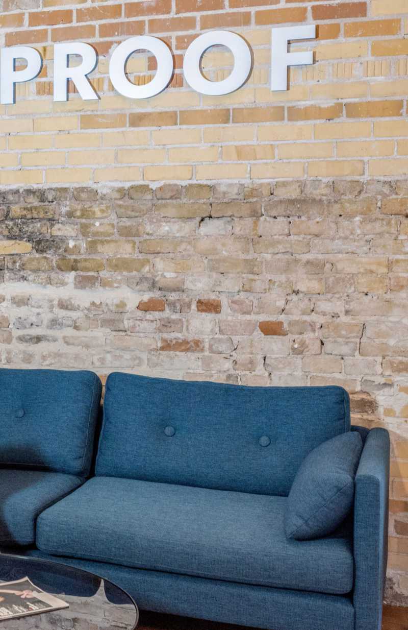Blaue Couch vor Ziegelwand mit dem Schriftzug "Proof". Ab und an lohnt es sich, eigene Kommunikation auf den Prüfstand zu legen. Katrin Walter - simply walter